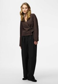 Brun wrapskjorte med lange ærmer og bindedetalje ved taljen, kombineret med sorte bukser med vide ben. Ensfarvet baggrund.