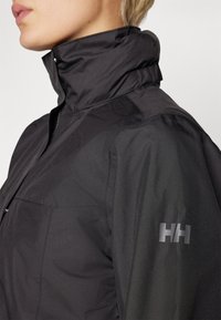 Black waterproof jacket with high collar, featuring smooth texture and "HH" logo on the left sleeve. Sleek design with visible stitching.