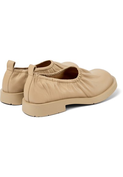 Beige läderslip-on skor med samlat elastiskt detalj vid öppningen, platt sula och rundad tå, med minimalistisk design.