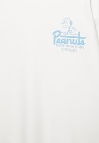 Valkoinen t-paita, jossa vasemmassa rinnassa vaaleansininen grafiikka, esittää piirroshahmo koiraa ja teksti "Peanuts Recreation and Leisure".