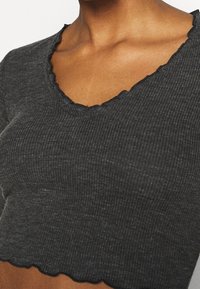 Szary krótki top z prążkowanej tkaniny; posiada karbowany dekolt w kształcie litery V i teksturowaną powierzchnię.