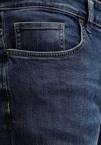 Granatowe dżinsy z tylną kieszenią, widocznym szyciem i subtelną teksturą z pionowymi liniami. Klasyczny pięcio-kieszeniowy krój.