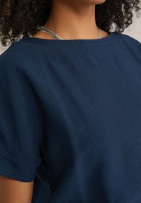 Top in lino blu navy con scollatura rotonda e maniche corte, caratterizzato da un tessuto leggermente testurizzato e dettagli di cucitura minimal.
