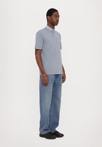 Light blue polo shirt with a slim fit, two buttons, short sleeves, paired with loose, medium wash denim jeans and black shoes.