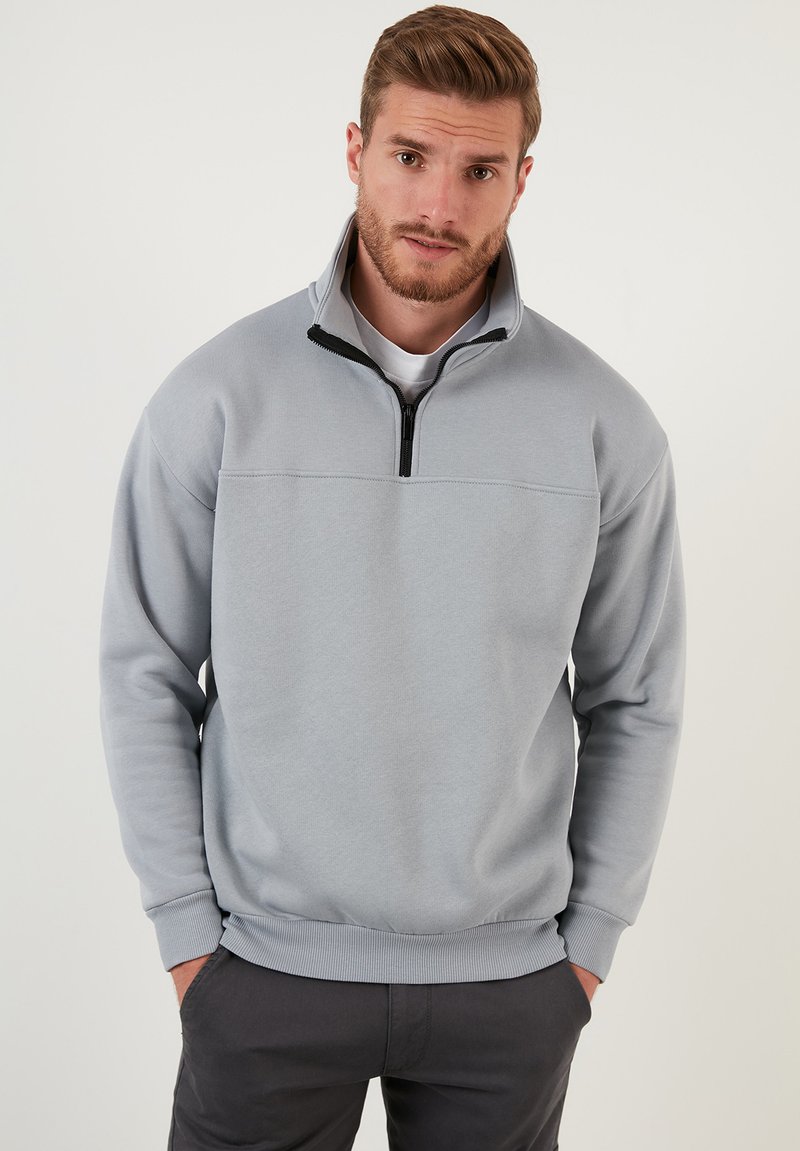 Sudadera de pullover gris claro con cuello de cremallera de cuarto, puños y dobladillo acanalados, hecha de una tela suave con una textura lisa.