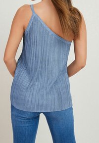 Canotta blu a costine con una sola spallina, che mostra un taglio rilassato e una texture morbida. Abbinata a pantaloni in denim blu.