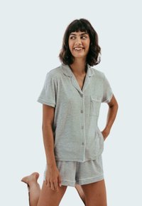 Harmaa puuvillapaita-asuste, joka koostuu lyhythihaisesta napitettavasta paidasta, jossa on tasku, ja vastaavista shortseista, joissa on valkoiset reunusyksityiskohdat.