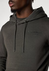 Donkergroen hoodie gemaakt van een katoenmix, voorzien van een kangoeroezak, verstelbare trekkoordcapuchon en een reliëflogo-detail aan de voorkant.