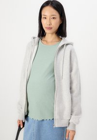 Ljusgrå zip-up hoodie med huva och ribbad krage, bärs över en mintgrön ribbad topp och kombineras med en denimkjol.