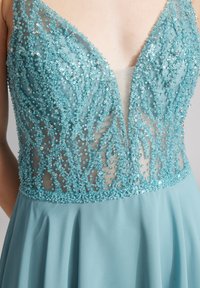 Ein hellblaues Kleid mit einem tiefen V-Ausschnitt, das mit aufwendigen Perlen- und Paillettenverzierungen am Oberteil sowie einem fließenden Rock ausgestattet ist.