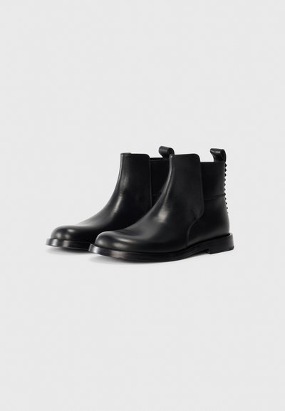 Botas Chelsea de cuero negro con una textura suave, puntera redonda, paneles laterales elásticos y un sutil detalle acanalado en el tacón.
