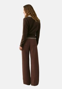 Maglione marrone a maglia con scollo a V e orlo a costine abbinato a pantaloni marroni a vita alta e larghi, con tasche laterali.