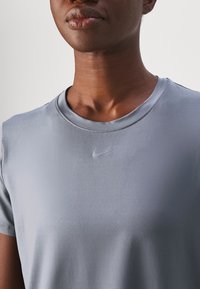 Primer plano de una persona que lleva una camiseta Nike de color gris claro, mostrando el cuello, los hombros y parte de la cara sin detalles de fondo visibles.