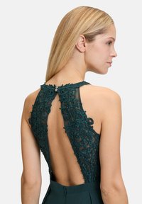 Türkises Kleid mit aufwendigen Spitzenakzenten auf dem Rücken, einem Schlüssellochdesign und glatter Stoffstruktur im gesamten Kleid.