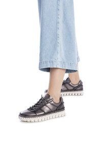 Zapatillas metálicas de color gris oscuro con suela de goma blanca, que presentan un patrón texturizado, adornos cosidos y cordones negros.