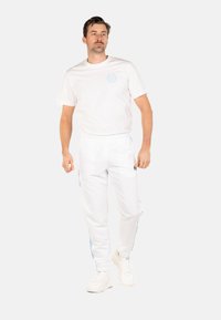 Tenue de sport blanche composée d'un t-shirt à manches courtes et de pantalons ajustés avec des rayures latérales bleu clair et un détail de logo. Baskets blanches.