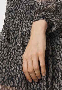 Šaty s černým a béžovým leopardím potiskem, průsvitnou látkou, nabíraným živůtkem a dlouhými nafouklými rukávy s knoflíky a ozdobnými detaily.