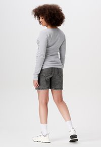 Graues Langarmoberteil kombiniert mit dunkelgrauen Jeansshorts. Das Modell trägt weiße Sneaker und Knöchelsocken. Glatter Stoff, lässige Passform, minimale Details.