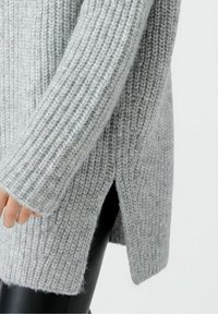 Pull en tricot gris avec une texture côtelée, doté de manches longues et d'ouvertures sur les côtés. Le matériau semble doux et confortable.