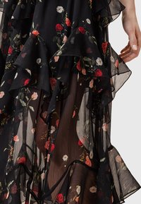 Black floral dress featuring ruffled layers, sheer texture, and a mix of red, pink, and white flowers printed on lightweight fabric.