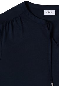 T-shirt bleu marine en tissu doux, avec un col rond, des épaules froncées et une courte fermeture éclair avant avec une garniture métallique.