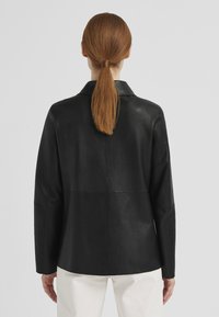 Schwarze Lederjacke mit schlankem Design, Reverskragen und langen Ärmeln; glatte Textur; Rückansicht zeigt gerade Nähte und minimale Details.