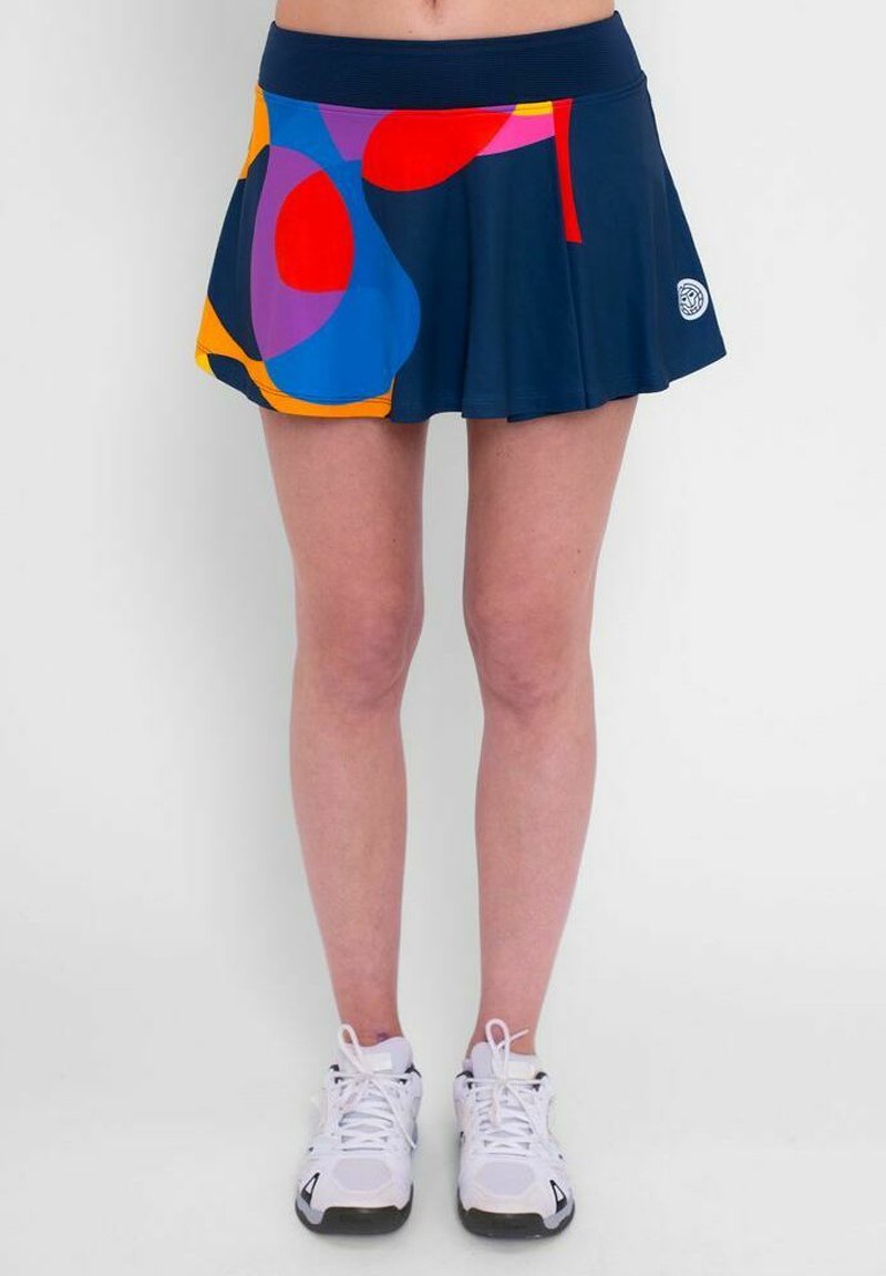Skort atlético navy con un patrón abstracto colorido (rojo, azul, amarillo, púrpura) y una cinturilla arrugada; combinado con zapatillas blancas.