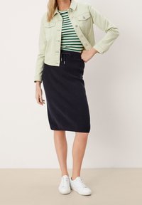 Gebreide marineblauwe pencil skirt met elastische tailleband, gecombineerd met een groen-gestreept shirt en een lichtgroene denimjas, gedragen met witte sneakers.