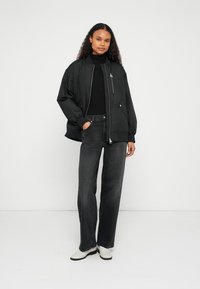 Μαύρο μπουφάν bomber με φερμουάρ μπροστά, συνδυασμένο με σκούρο γκρι παντελόνι φαρδύ στο πόδι και λευκά μποτάκια στον αστράγαλο. Το μπουφάν διαθέτει ριμπ μανσέτες και τσέπες.