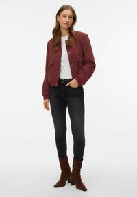 Blouson aviateur bordeaux avec deux poches frontales, porté sur un haut blanc. Associé à un jean skinny noir et des bottines en daim marron.