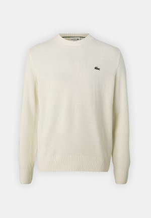 Maglione color crema realizzato in morbido materiale a maglia, con scollo rotondo, polsini a coste e un piccolo logo verde sul petto.