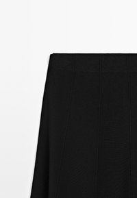 Gonna in maglia nera con texture a coste verticali, cintura aderente e lunghezza midi senza ulteriori decorazioni.
