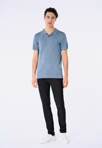 Camisa polo de manga corta en azul claro con textura de punto y dobladillo acanalado, combinada con pantalones slim-fit negros y zapatillas blancas.