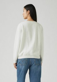 Sweatshirt gris clair avec un col rond, des poignets et un ourlet côtelés. Associé à un jean en denim bleu avec des coutures discrètes sur les poches.