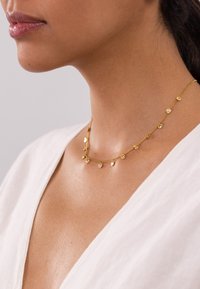 Goldkette mit kleinen, runden Anhängern, zartem Kettendesign und glatter Oberfläche, getragen auf einem neutralen, strukturierten Stoff.