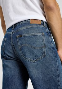 Jeans de mezclilla azul oscuro con corte recto, doble bolsillo trasero con detalle de costura y una parche de cuero con marca en la cintura.