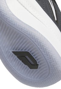 Svart sportskosula med en strukturerad vit yttersula. Har ett geometriskt mönster och ett svart emblem i mitten.