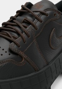 Czarne skórzane sneakersy z brązowym przeszyciem i sznurowadłami, z teksturowaną podeszwą oraz logo Nike w kształcie znaku "swoosh" po boku.