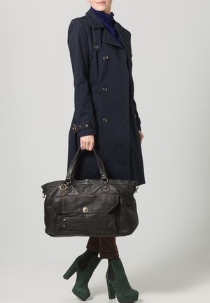 Schwarze Ledertasche mit einem vorderen Reißverschlussfach, doppelten Tragegriffen und goldenen Hardware-Details. Das Modell kombinierte sie mit einem marineblauen Mantel und grünen Schuhen.