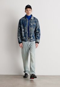 Τζάκετ από τζιν με υφασμάτινο μπλε σχέδιο, φορεμένο πάνω από μπλε ζιβάγκο, συνδυασμένο με ανοιχτόχρωμα τζιν και μαύρα παπούτσια. Καθημερινό καπέλο στο κεφάλι.