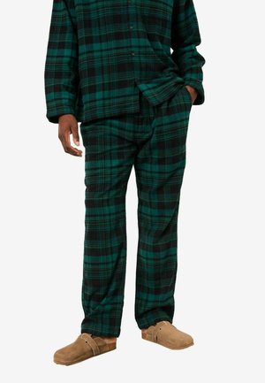 Grüne und schwarze karierte Flanellpyjamas mit einem knöpfbaren Oberteil und lockeren Hosen, ergänzt durch braune Wildlederschlupfschuhe.