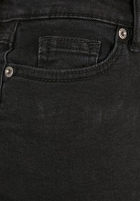 Gros plan sur un jean en denim noir montrant la poche avant, la petite poche et deux rivets métalliques avec des détails de couture.