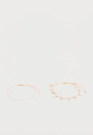 Two delicate gold chain bracelets, one with small pearls, the other with pearl and crystal charms, laid flat on a pale surface.