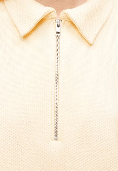 Κρεμ χρωματιστό φούτερ με φερμουάρ και υφή υφάσματος, με γιακά και μεταλλικό φερμουάρ στο μπροστινό μέρος. Απλός σχεδιασμός χωρίς σχέδια.