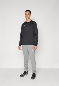 Svart langermet treningsskjorte med en subtil logo, kombinert med grå joggebukser med oppbrettede ankler og en logo på siden. Svarte treningssko.