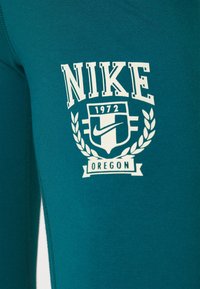Teal idrottsstoff med en vit Nike-logotyp och emblem med "1972" och "OREGON." Designen inkluderar lagerkrans-accenter och blockbokstäver.