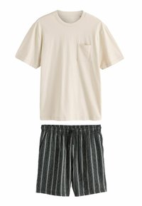 Beige Baumwoll-T-Shirt mit kurzen Ärmeln und einer Brusttasche, kombiniert mit schwarzen gestreiften Shorts mit Kordelzug und einem elastischen Bund.