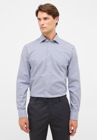 Camicia a righe blu e bianche con maniche lunghe, frontale abbottonato e colletto, realizzata in un tessuto morbido, abbinata a pantaloni scuri.
