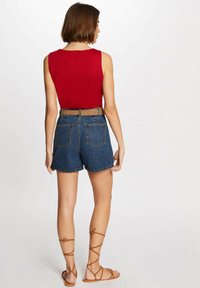 Rotes ärmelloses Oberteil kombiniert mit hochgeschnittenen Jeansshorts und brauem Gürtel; Modell trägt beige Gladiatorensandalen, Rückansicht gezeigt.