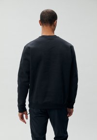 Sweatshirt en coton noir avec un col rond, des poignets côtelés et une coupe décontractée. Texture lisse sans motifs ni accents visibles.